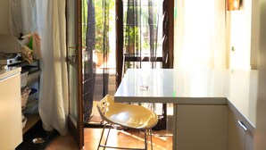Une cuisine avec un coin repas, une petite table et une chaise. On y trouve une fenêtre avec des rideaux, un évier et un placard.