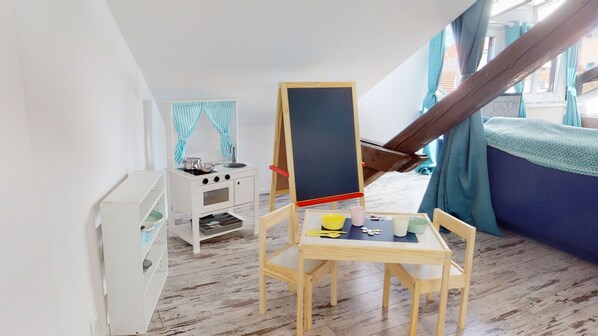 A child's playroom with a wooden play kitchen, a chalkboard, and a blue sofa.