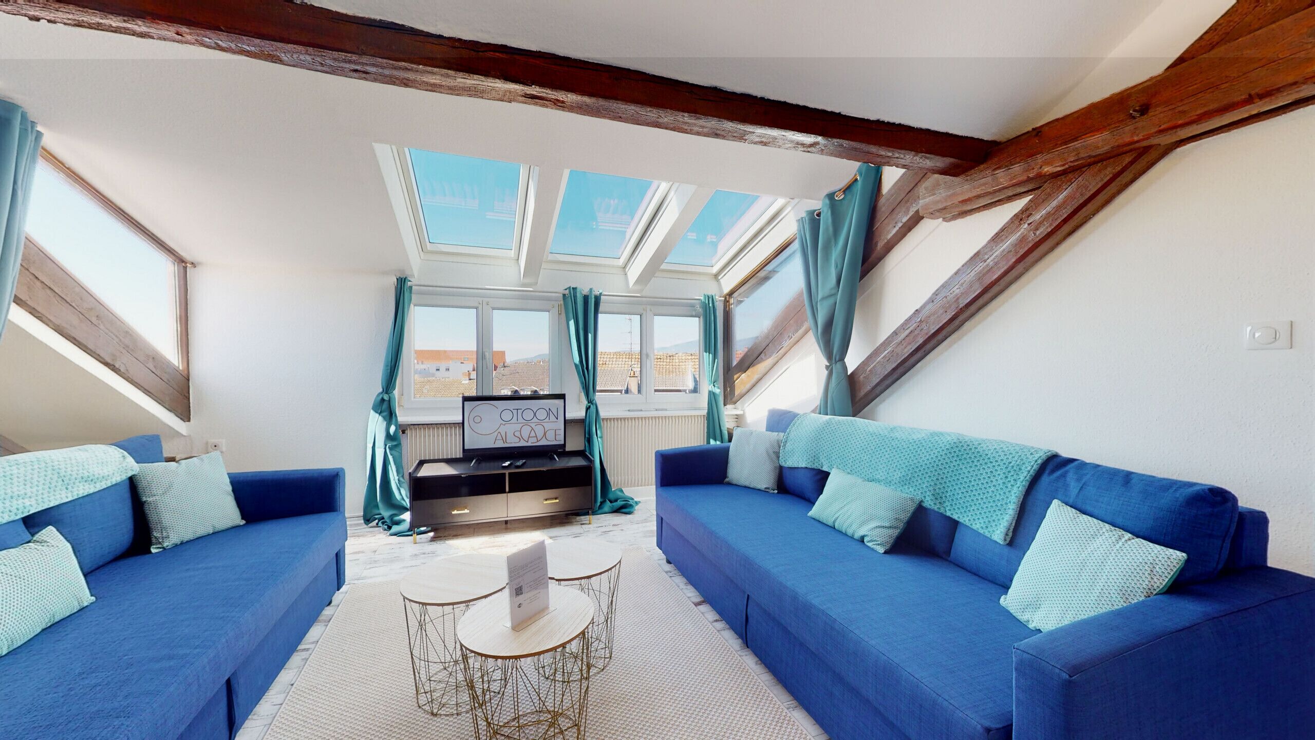Een kamer met een blauwe zithoek, een bijzettafeltje en een tv op een meubel.