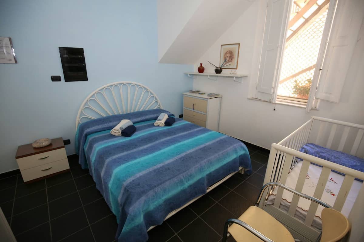 Un dormitorio con cama, mesita de noche, cómoda, cuna y ventana con vistas.