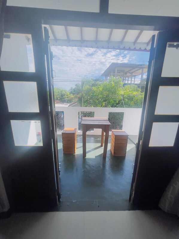 An open doorway leading to a balcony with a table and two wooden stools.