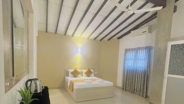 A hotel room with a bed, a bedside table with a kettle, a plant, and a mirror. - Chrish Residence (Negombo)