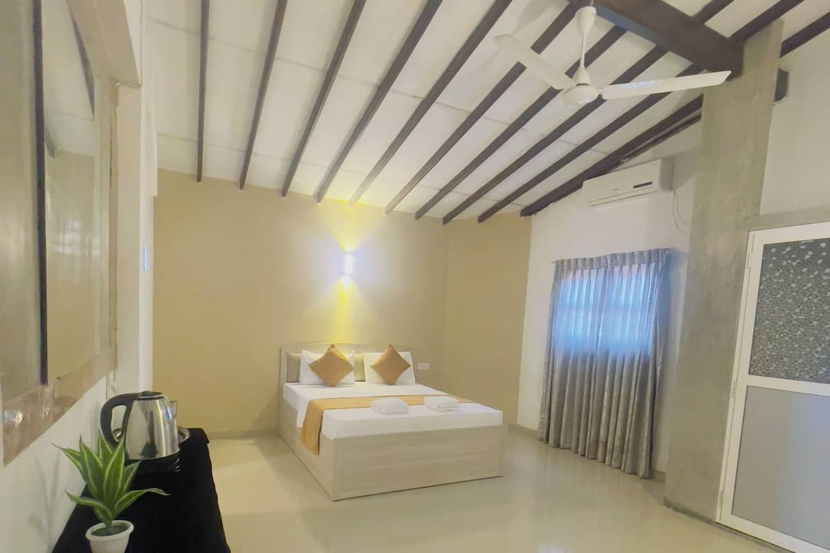 A hotel room with a bed, a bedside table with a kettle, a plant, and a remote control.