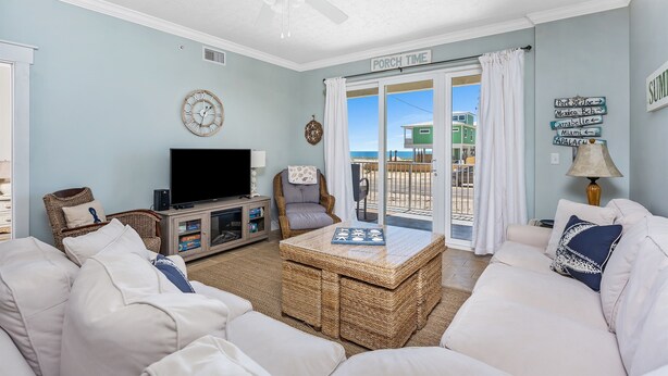 A living room with a television, wicker furniture, a sign reading "PORCH TIME", and a view of the ocean.