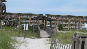 A wooden pathway leading to a beachside building with multiple balconies.