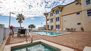 A pool area with two pools, lounge chairs, and a building with multiple windows.