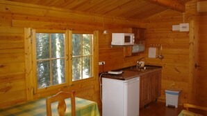 En stuga byggd av trä med ett köksutrymme, ett matbord med en rutig duk och ett fönster med utsikt över träd.