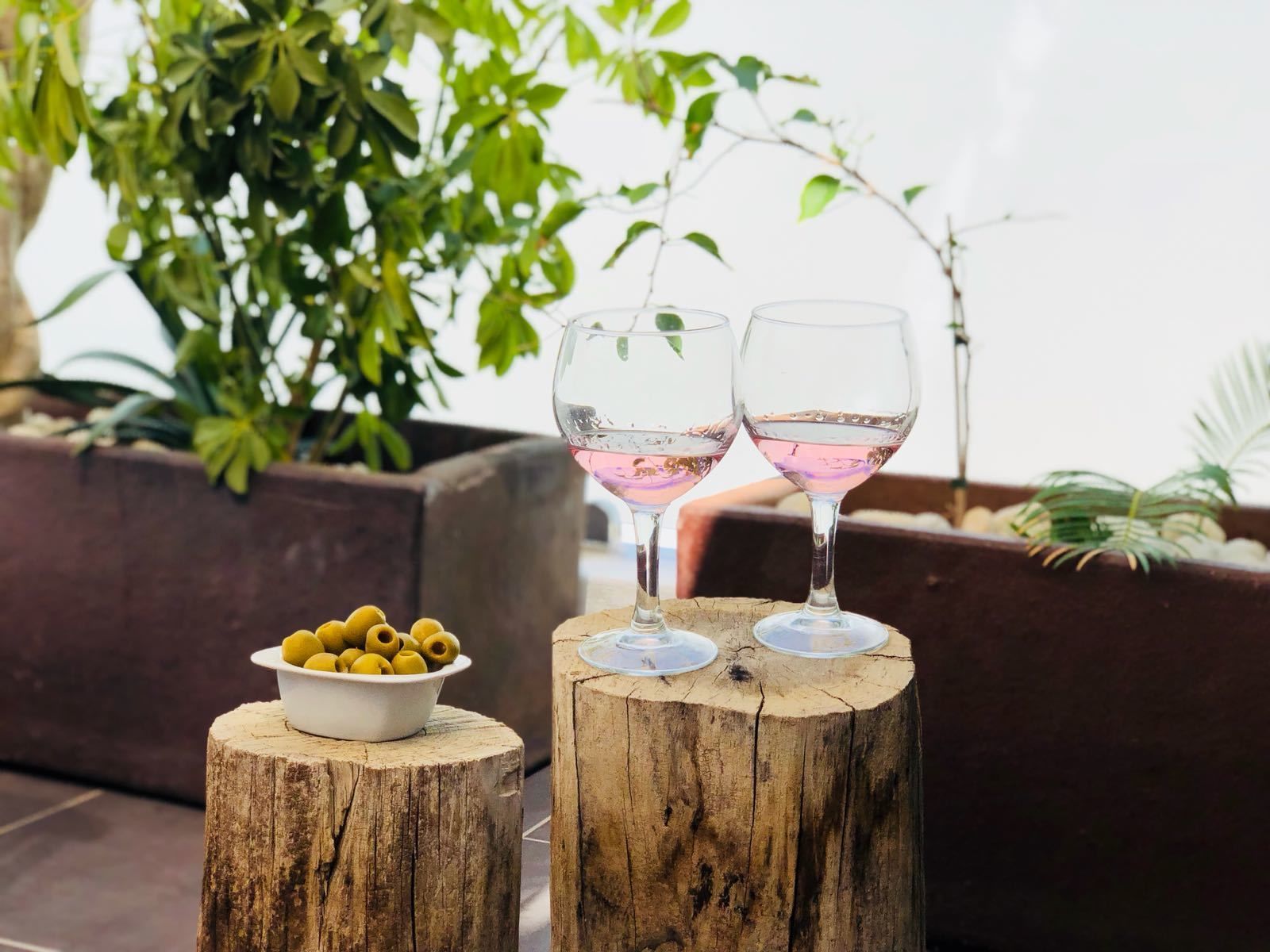 Two glasses of pink drink on wooden stools with a bowl of olives on one.