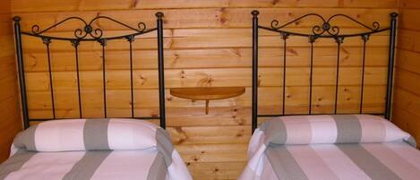 Una habitación con dos camas, paredes de madera y un pequeño estante.
