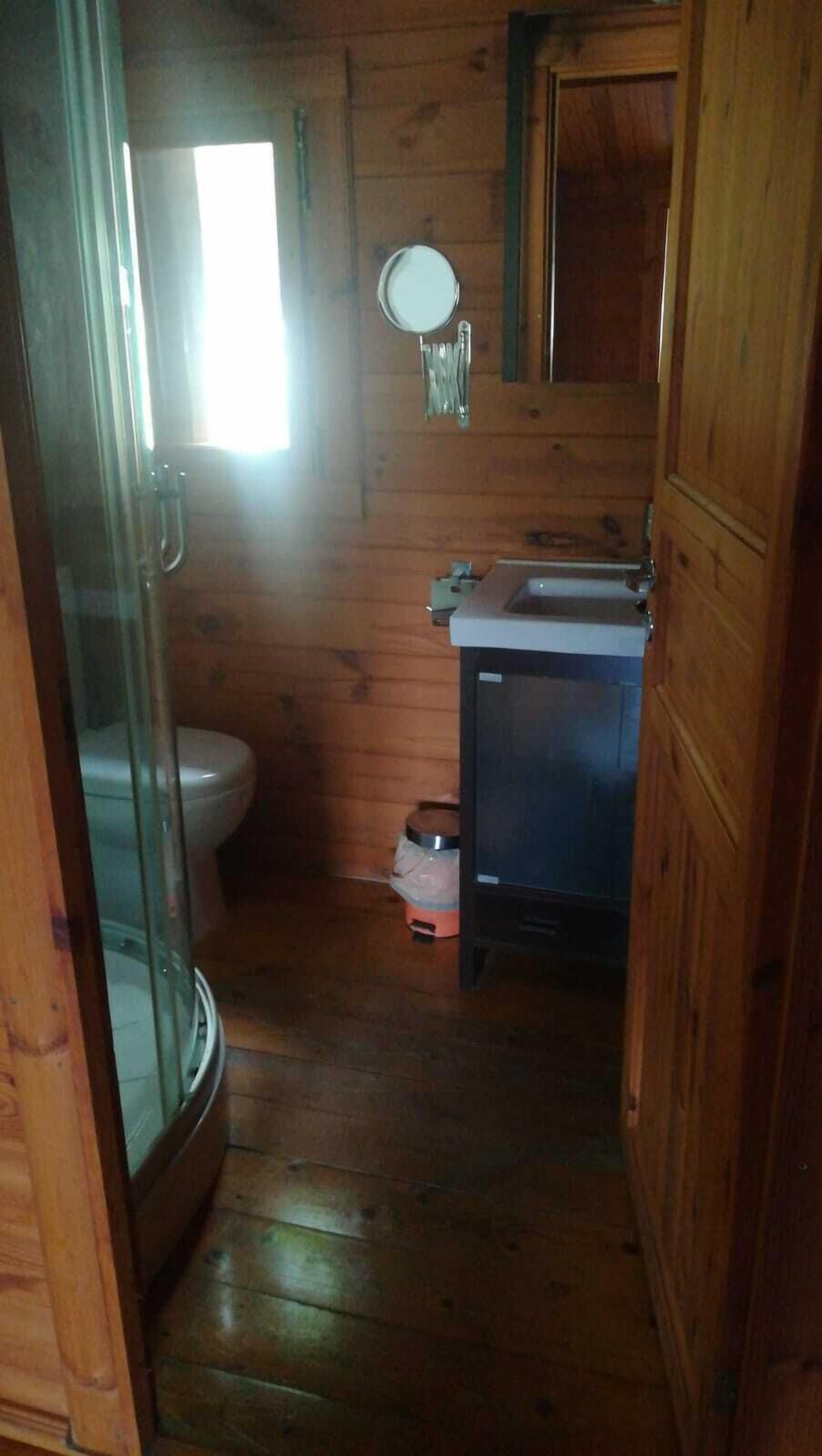 Une salle de bain rustique, aménagée dans une cabane en bois, avec des toilettes, un lavabo et un miroir.