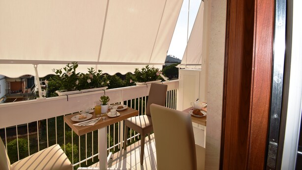 Un balcon avec une table dressée pour le petit-déjeuner, des plantes en pot et une vue sur les environs.