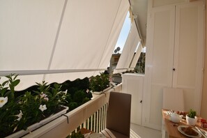 A balcony with potted plants, a chair, and a table with a teapot and pastries. - Melody Sorrento Suites (Sorrento)