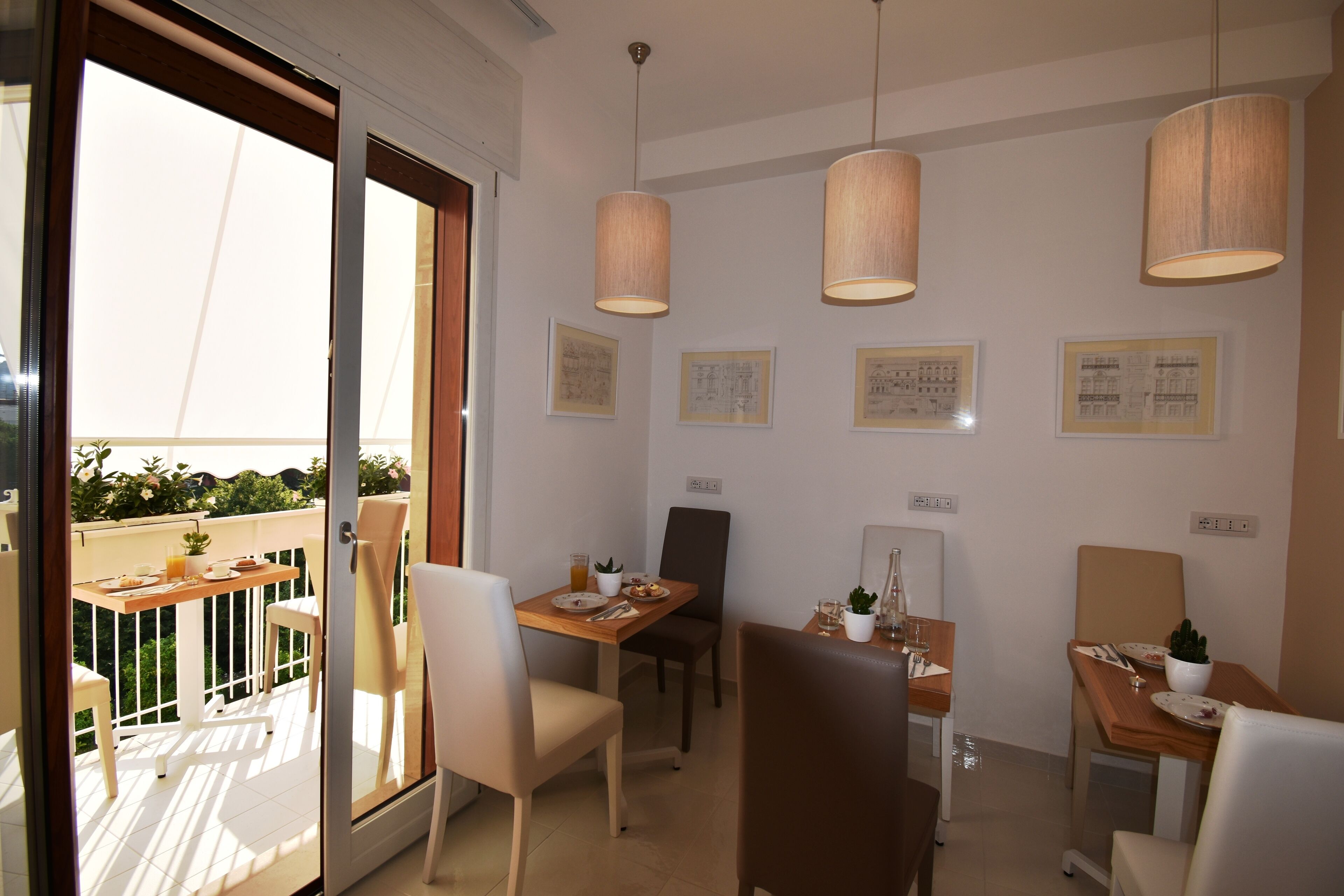 A dining area with two tables, chairs, pendant lights, and framed artwork on the walls.