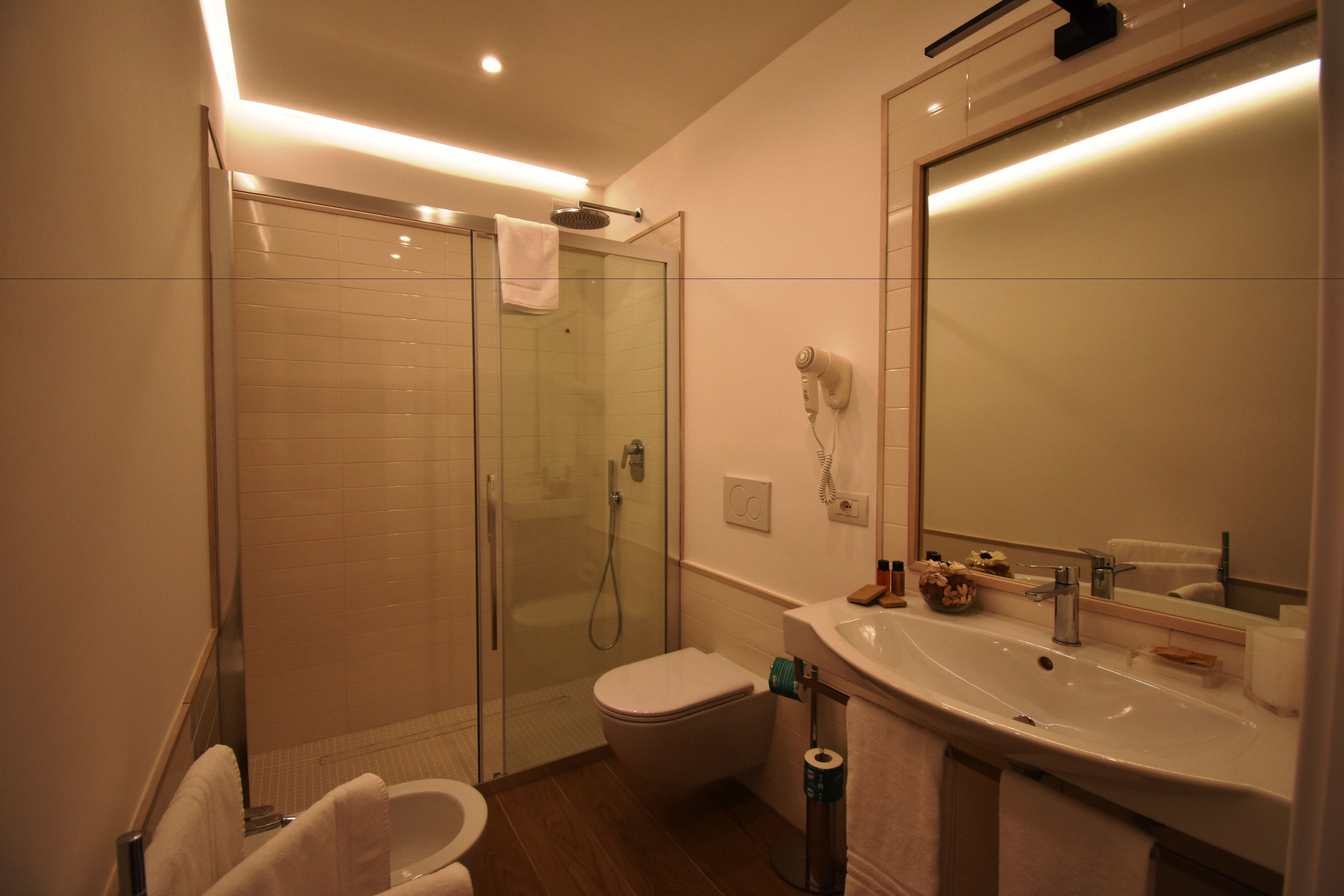 Un bagno moderno con cabina doccia in vetro, un water, un lavandino e uno specchio grande.