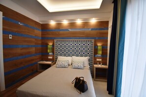 A hotel room with a large bed, wooden panel walls, patterned headboard, bedside lamps, and a handbag on the bed. - Melody Sorrento Suites (Sorrento)