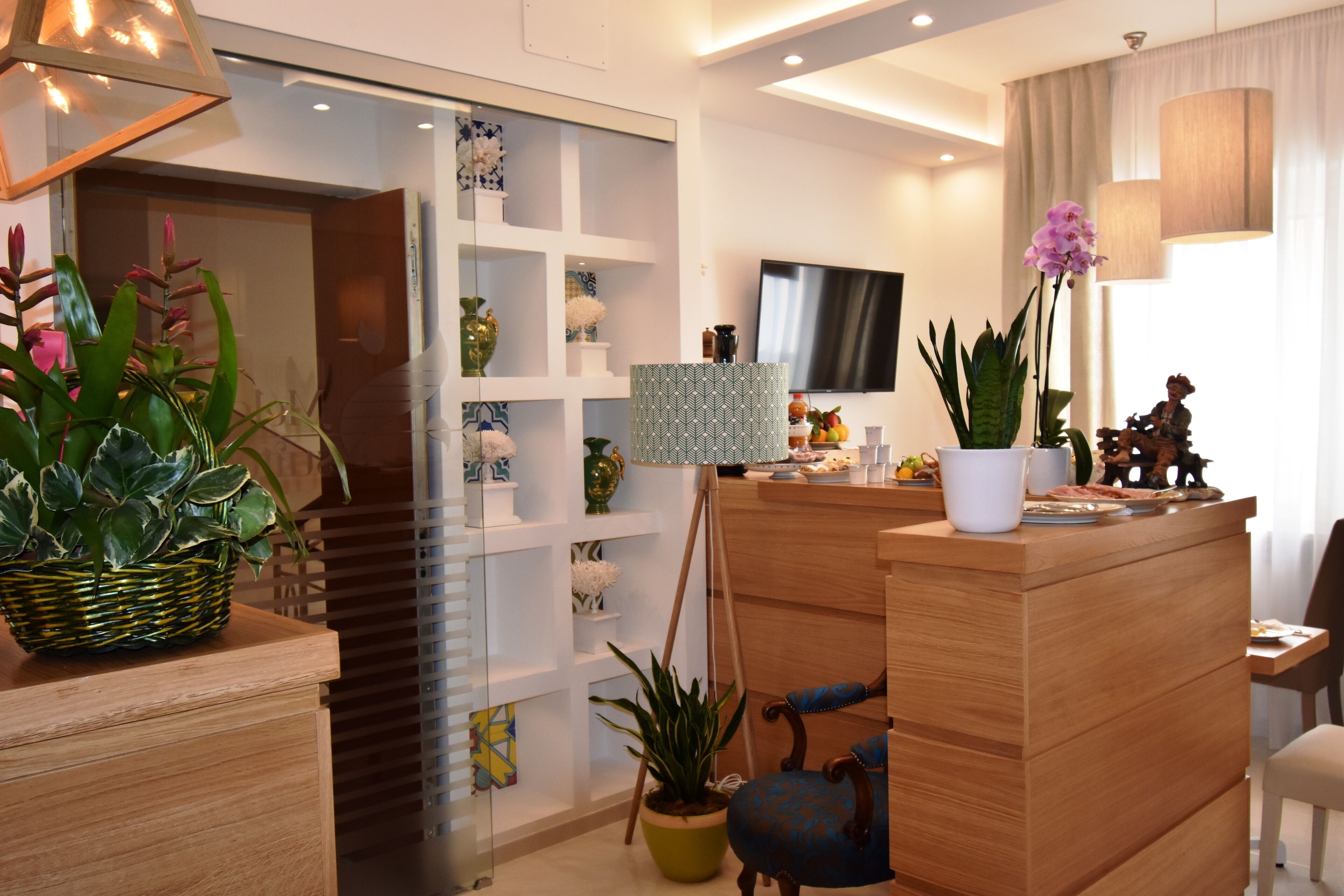 A modern living room with a wooden reception desk, a television, and various decorative items including plants and figurines.
