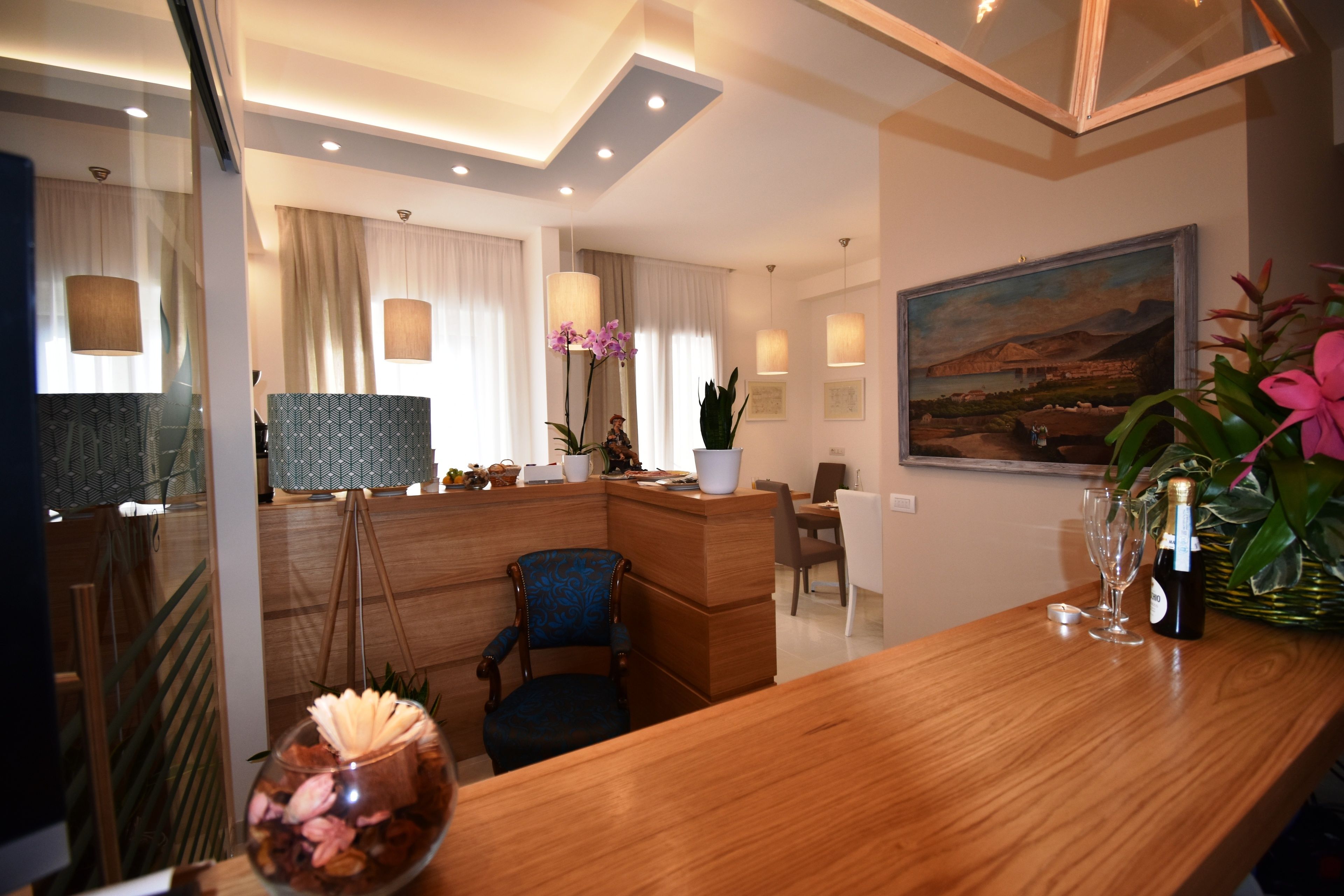 A modern hotel lobby with a wooden reception desk, a seating area, and a large painting on the wall.