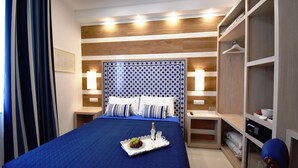 Une chambre d’hôtel avec un grand lit, une table de chevet avec une lampe, une armoire et un plateau avec des fruits et une bouteille posés sur le lit.