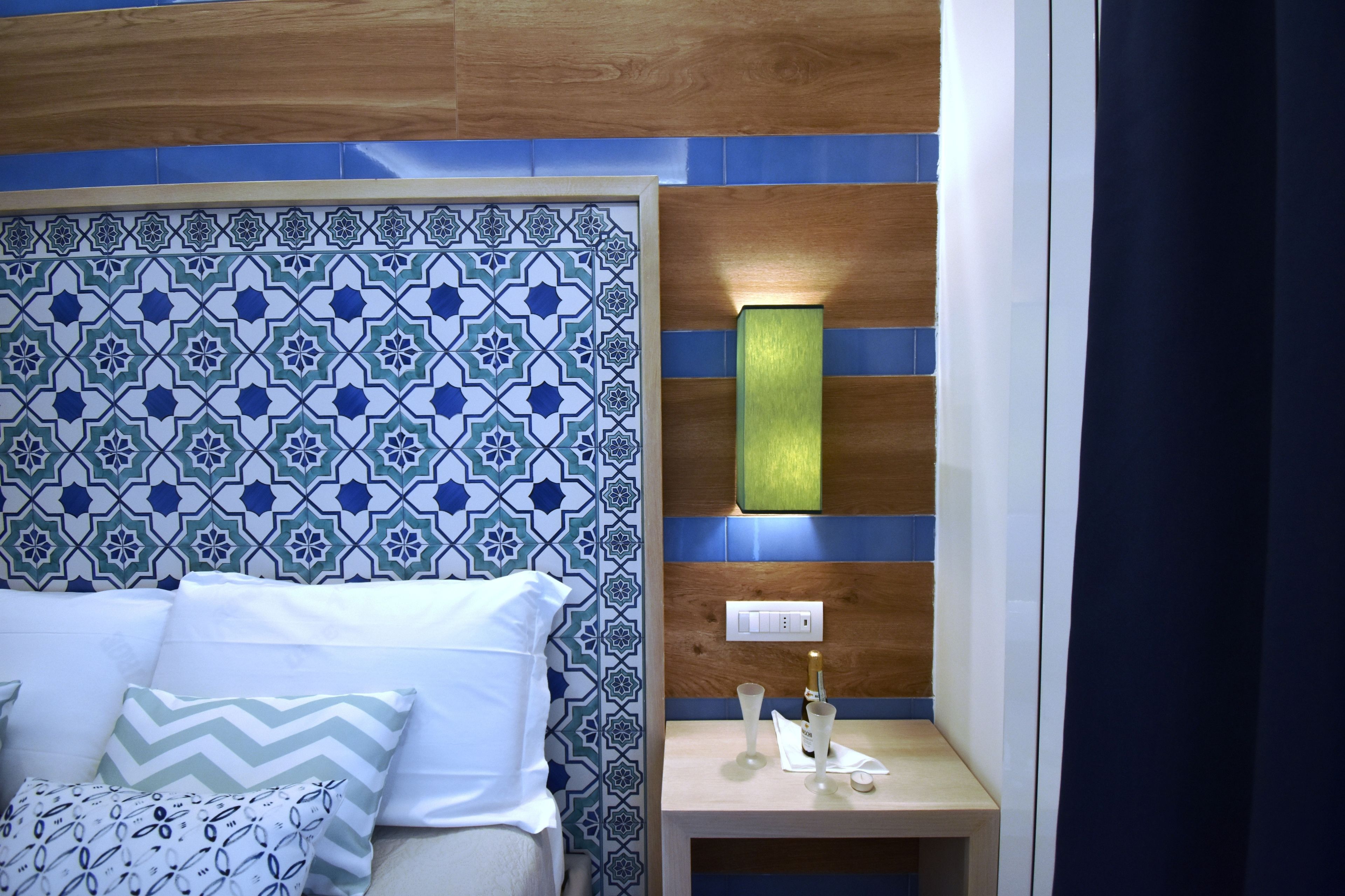 Une chambre à coucher avec une tête de lit à motifs, une table de chevet avec une bouteille et des verres, et une prise électrique.