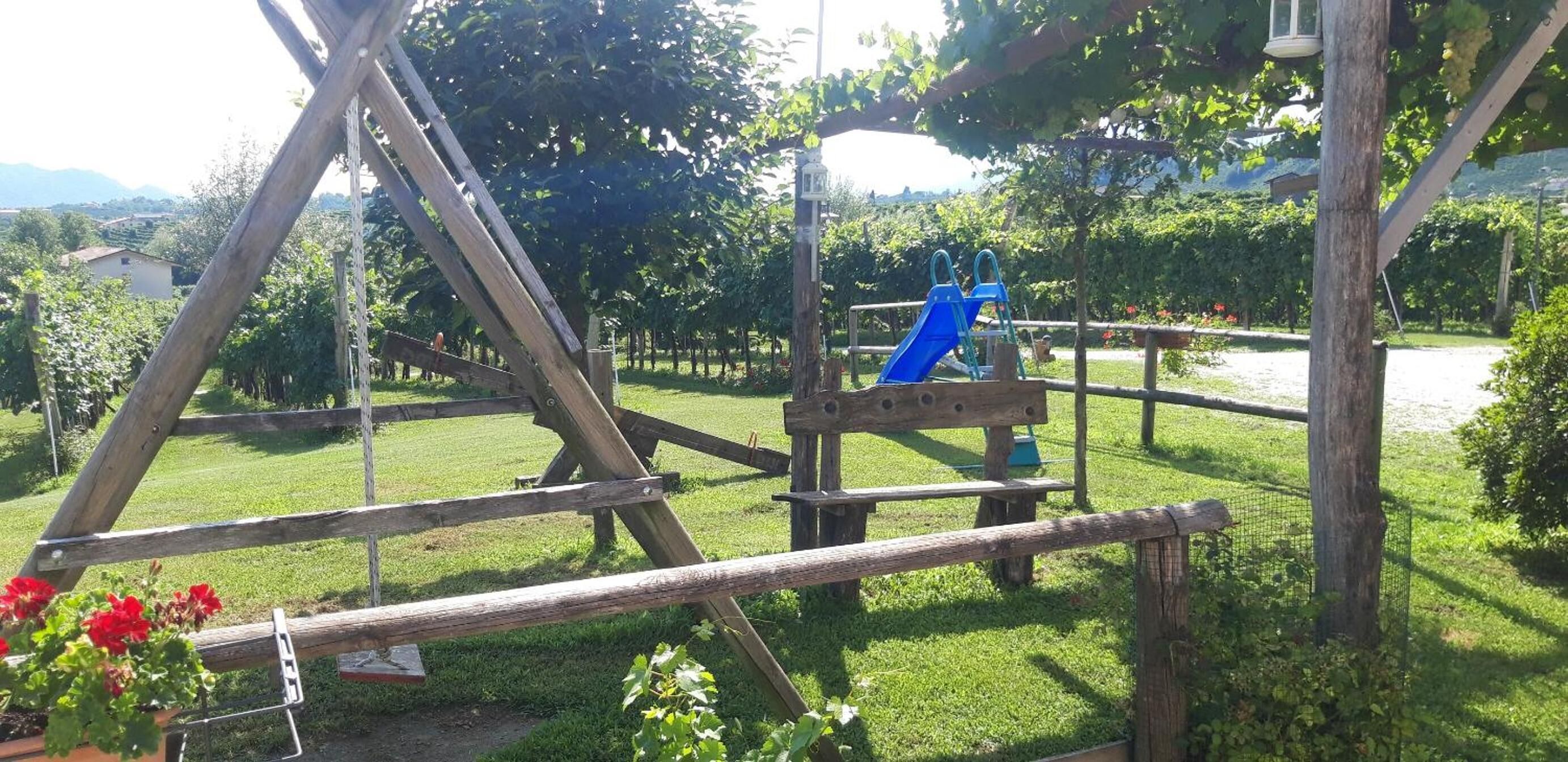 Una struttura in legno rustica con uno scivolo blu, immersa nel verde sotto un cielo sereno.