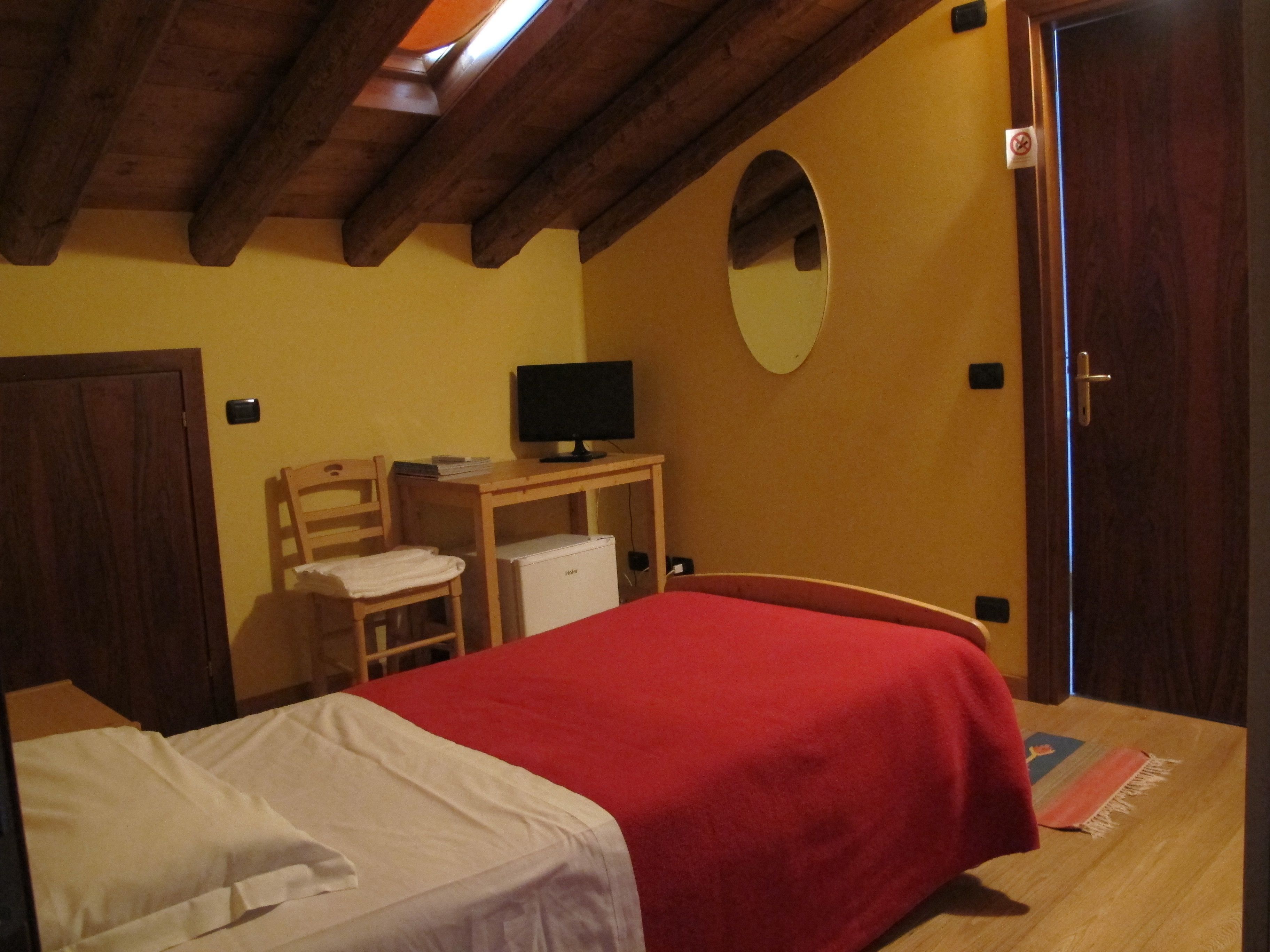 Een slaapkamer met een bed, een bureau met een computer, een spiegel en een deur.