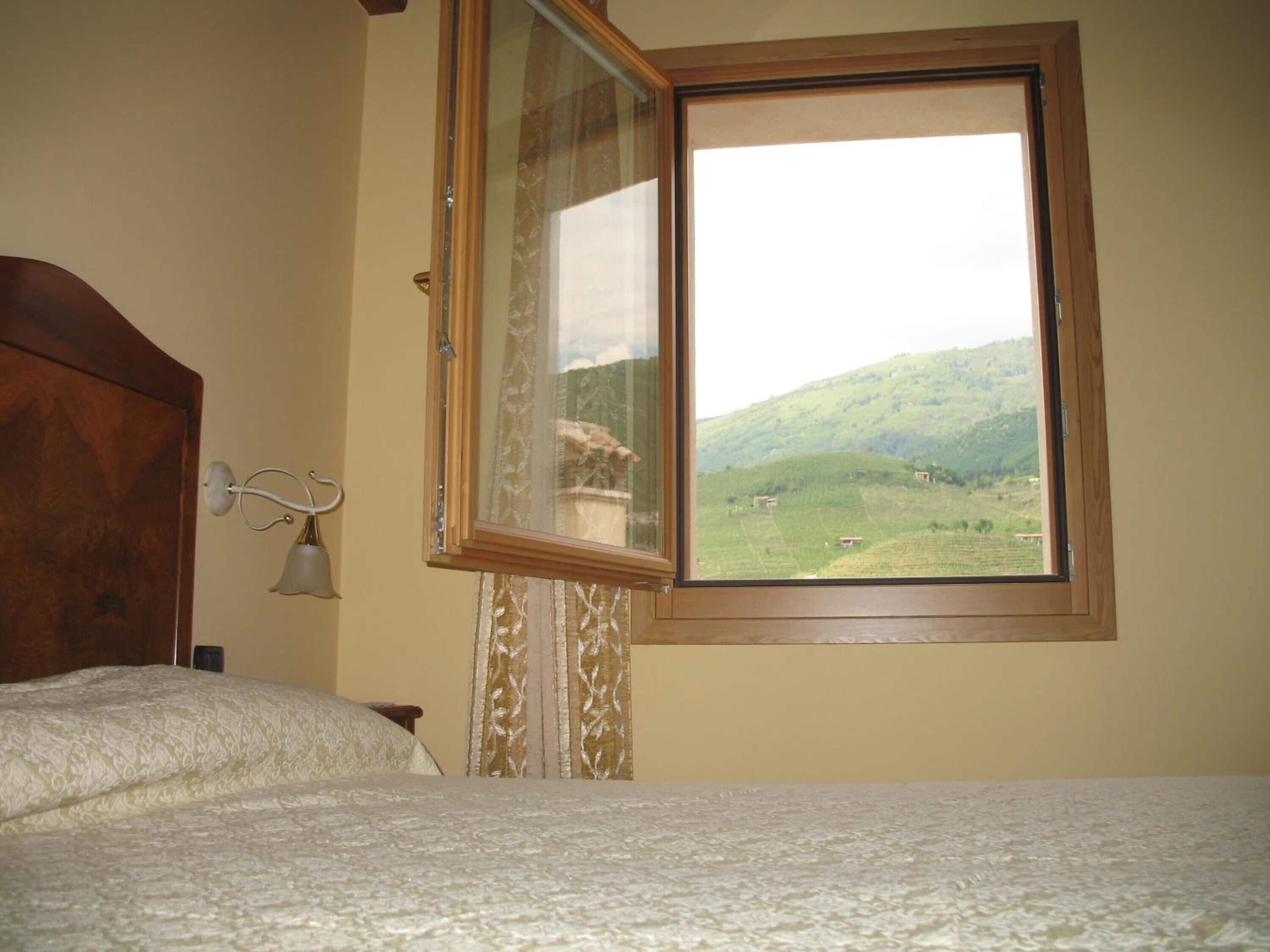 Una camera da letto con un letto, una finestra vista su un paesaggio verde e una testiera in legno.