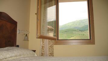 Una camera da letto con un letto, una finestra vista su un paesaggio verde e una testiera in legno.