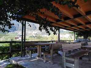 Un espace extérieur abrité, doté de bancs, offrant une vue sur un paysage montagneux et un village situé en contrebas.