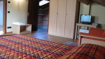 A bedroom with a bed, a wooden wardrobe, a television on a small table, and a bathroom visible through an open door.