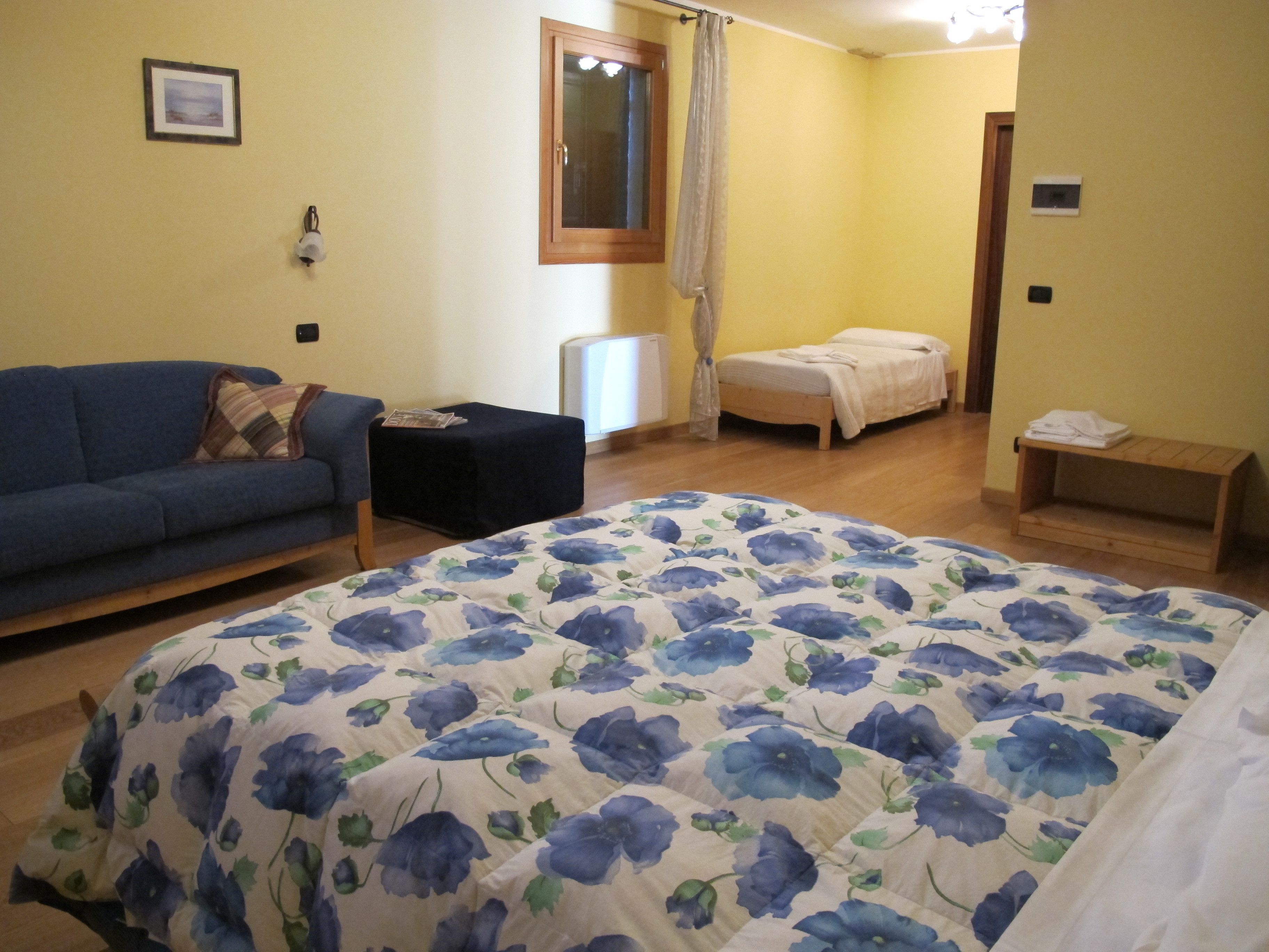 Une chambre à coucher avec une couvre-lit à motifs floraux, un canapé, une table de chevet et une petite étagère en bois.