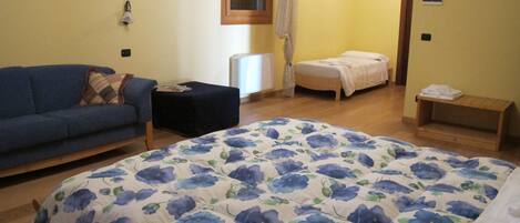 Une chambre à coucher avec une couvre-lit à motifs floraux, un canapé, une table de chevet et une petite étagère en bois.