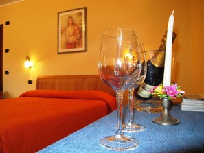 Une chambre d’hôtel avec un lit, deux verres à vin, une bougie et un tableau encadré au mur.