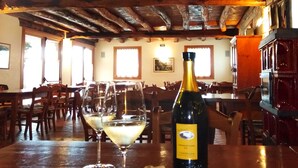 A restaurant interior with wooden beams on the ceiling, tables with chairs, and a bottle of wine on the table.