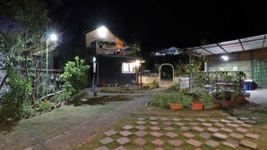 A two-story building with a balcony, surrounded by a garden with potted plants and a paved walkway. - Cottages at Village (Nainital)