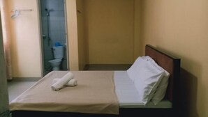 Una habitación pequeña con una cama individual, cabecera de madera, colcha color beige y almohada blanca. Hay una toalla sobre la cama.