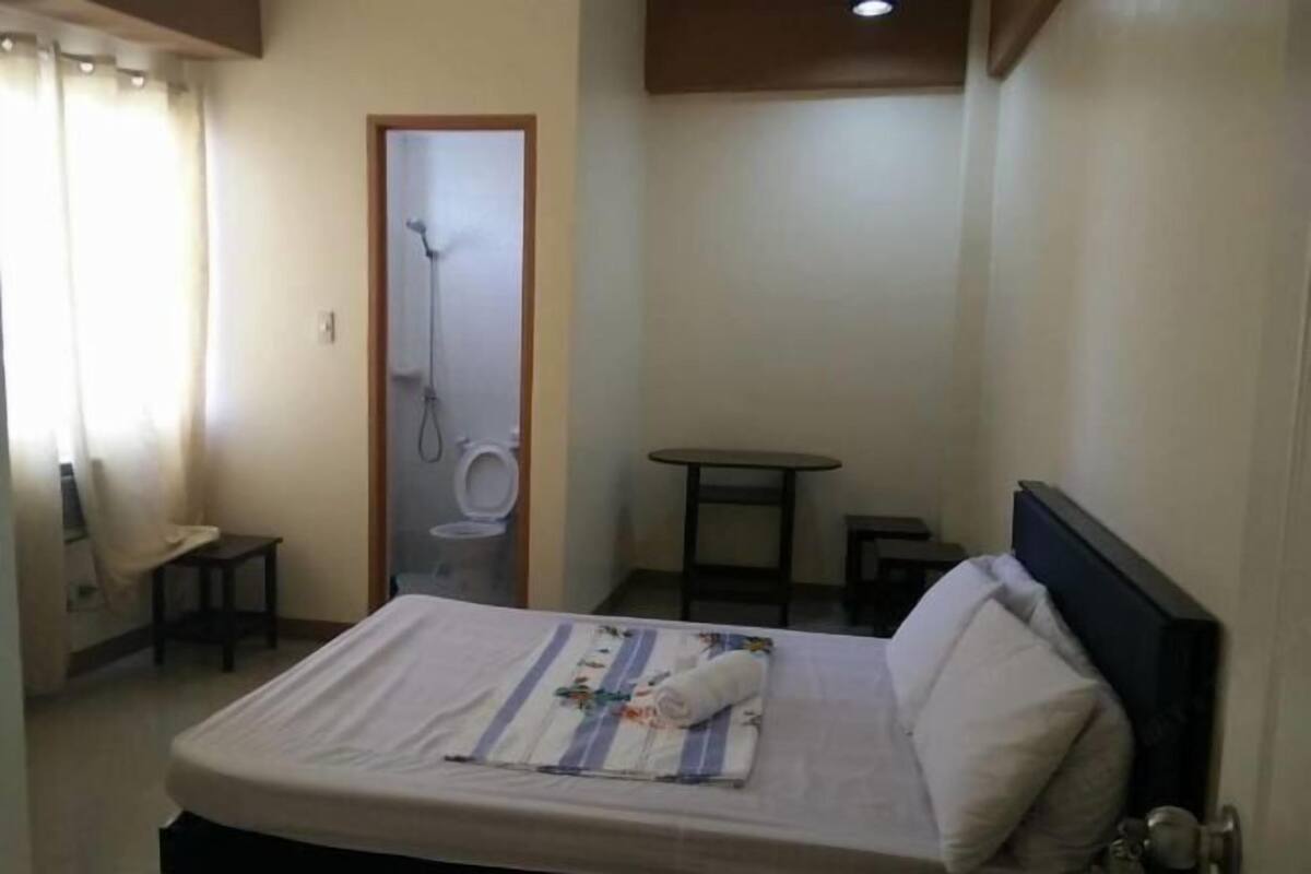 Una habitación pequeña y limpia con cama, una mesita, una silla y zona de ducha.