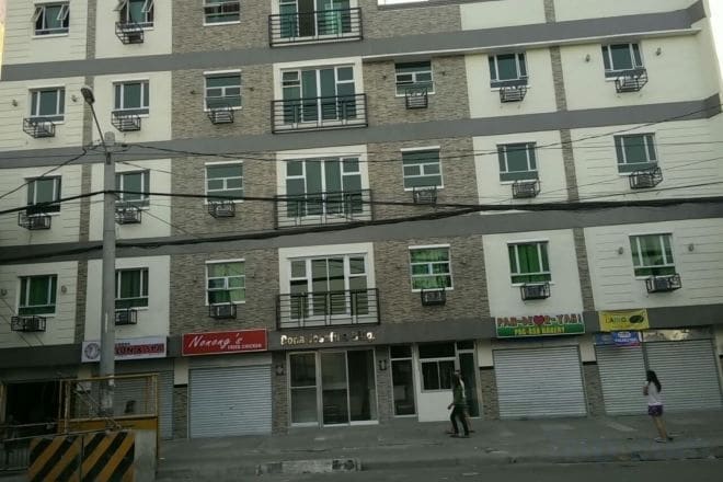 A multi-story building with several ground-level commercial spaces, including a visible storefront with a sign.