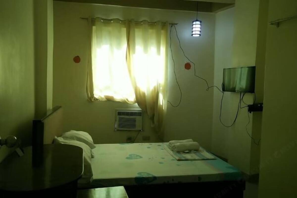 Una habitación con cama, escritorio, televisor y ventana con cortinas.