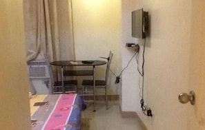 A small room with a single round table and two chairs, a television mounted on the wall, and a door with a round knob.