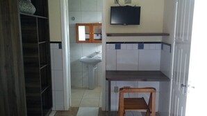 Una cocina compacta con un lavamanos, una silla de madera y un televisor montado en la pared.