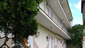 Un edificio de varios pisos con balcones, un césped cuidado y plantas tropicales.