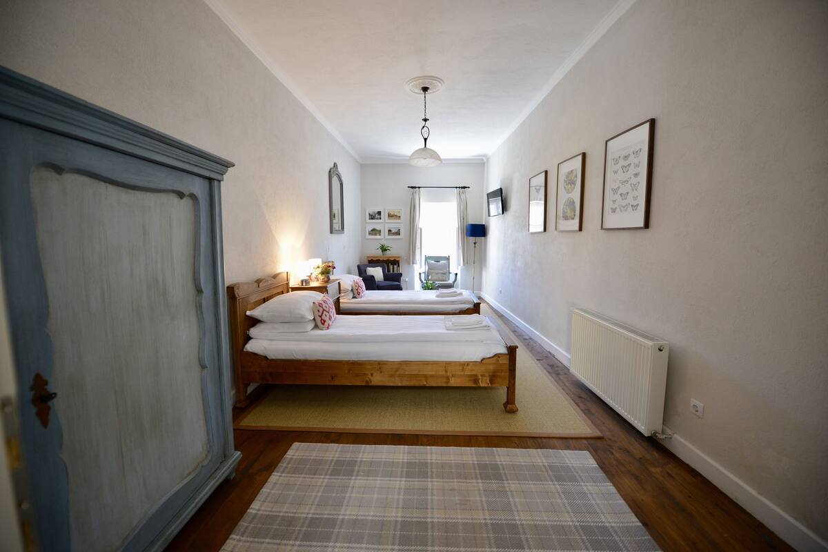 A bedroom with two wooden beds, a wardrobe, a radiator, and framed pictures on the wall.