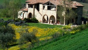 A stone house with a tiled roof, arched windows, and a garden with yellow flowers. - Agriturismo Pian di Frattina (Fabro)