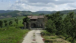 A gravel path leading to a stone building with a tiled roof, surrounded by green fields and hills. - Agriturismo Pian di Frattina (Fabro)