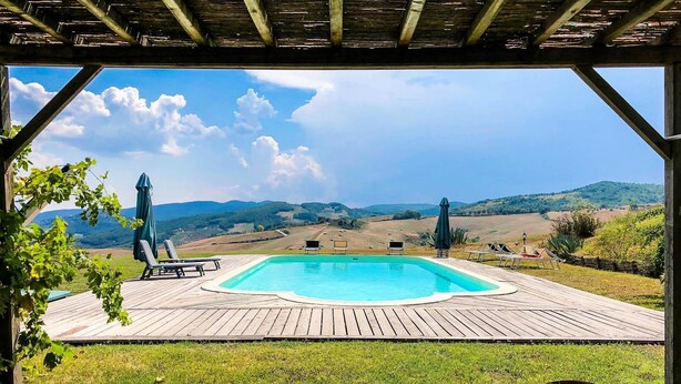 A wooden deck with a swimming pool, lounge chairs, and a view of rolling hills. - Agriturismo Pian di Frattina (Fabro)