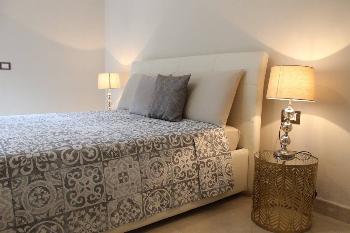 Un dormitorio con una cama, dos lámparas de noche y una mesita decorativa.