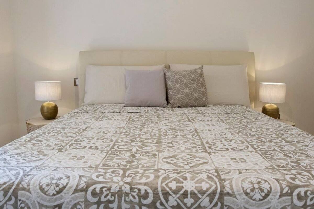 Un dormitorio con una cama grande, dos lámparas de noche y una colcha estampada.