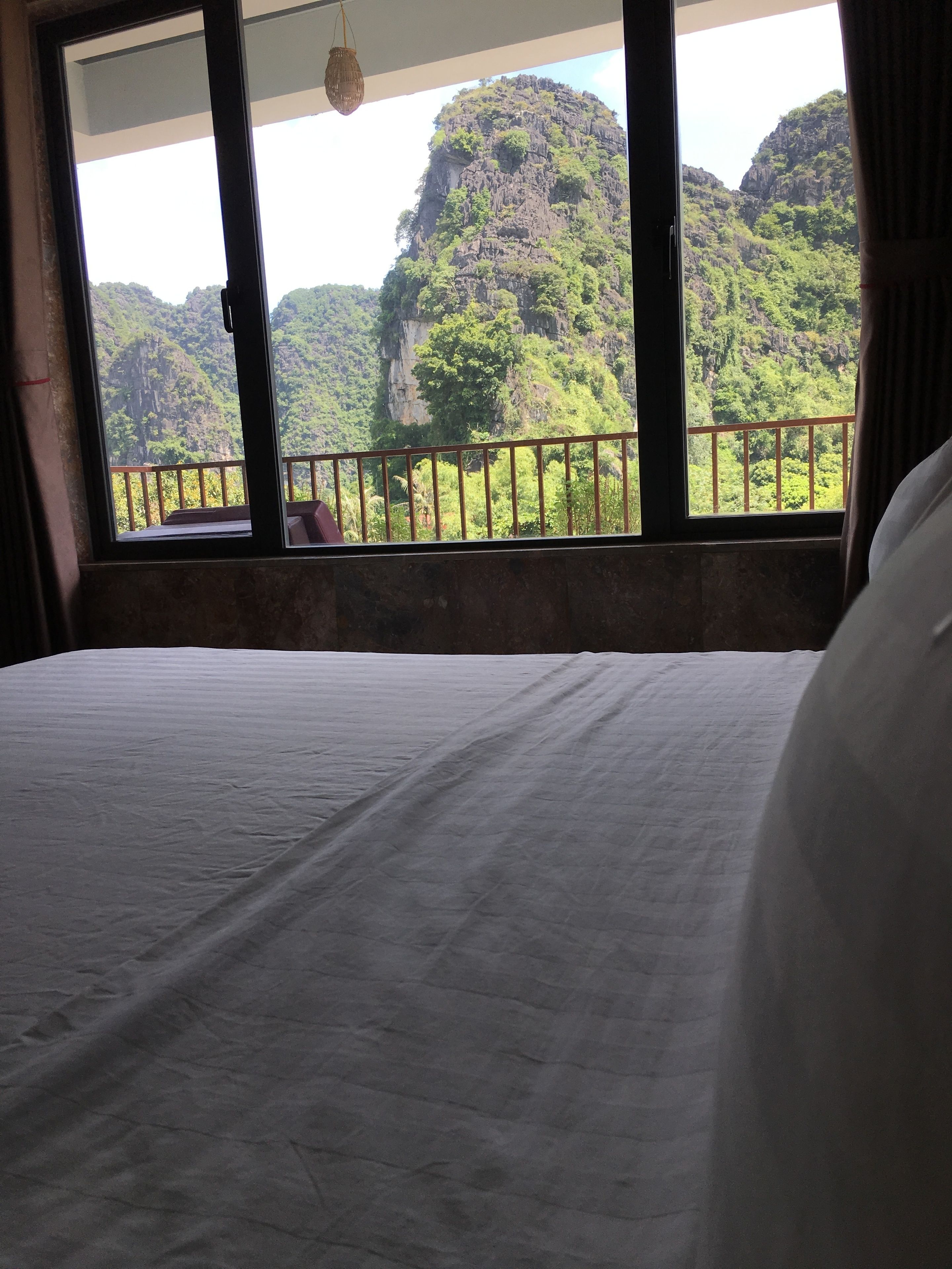 A bed with a view of a mountainous landscape through a window with a metal railing.
