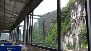 A room with large windows offering a view of a rocky cliff and lush greenery. - Limestone Boutique Hotel (Ninh Binh)
