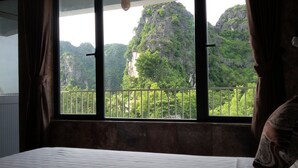 A room with a bed, a window with a view of a mountainous landscape. - Limestone Boutique Hotel (Ninh Binh)